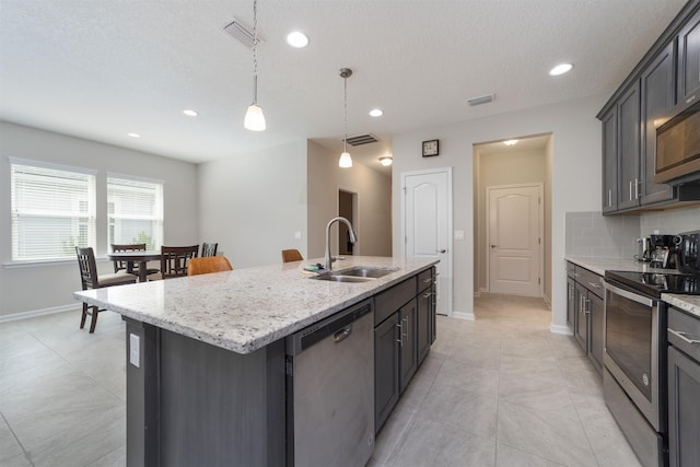 kitchen featuring sink, pendant lighting, a textured ceiling, a kitchen island with sink, and appliances with stainless steel finishes