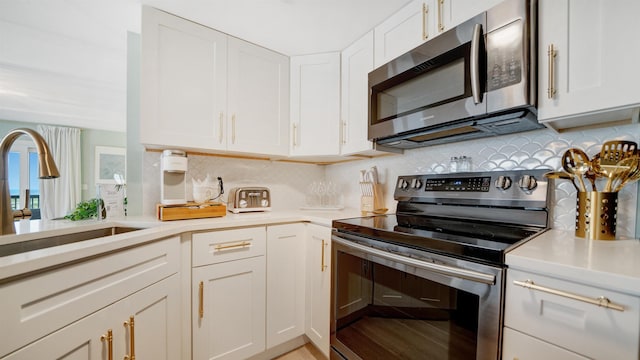 kitchen featuring stainless steel appliances, light countertops, a sink, and white cabinetry