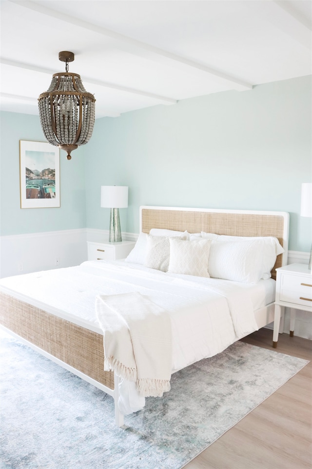 bedroom featuring wood finished floors, beam ceiling, and an inviting chandelier