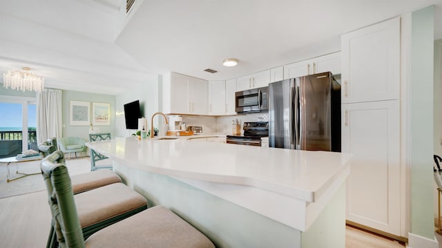 kitchen featuring a breakfast bar area, stainless steel appliances, white cabinetry, open floor plan, and light countertops