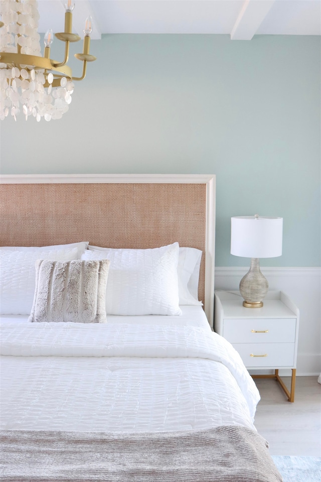 bedroom featuring beamed ceiling, wood finished floors, and an inviting chandelier