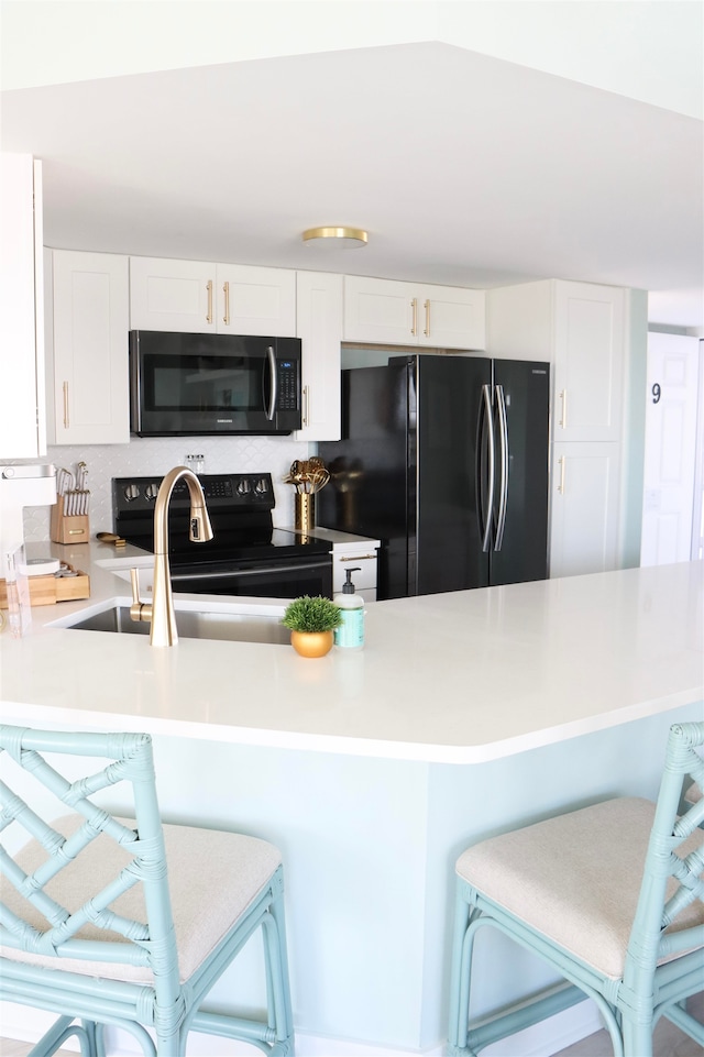 kitchen with a kitchen bar, light countertops, white cabinetry, and black appliances