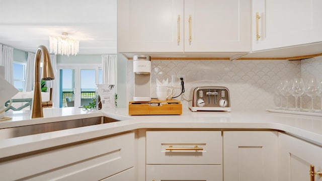 kitchen with tasteful backsplash, white cabinets, light countertops, a chandelier, and a sink