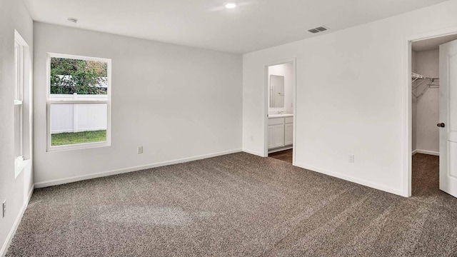 unfurnished bedroom featuring dark carpet, sink, a spacious closet, connected bathroom, and a closet