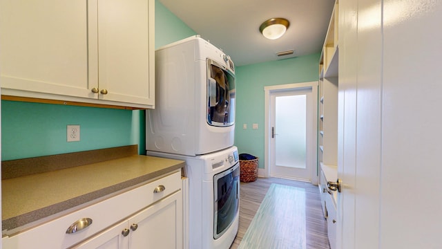 clothes washing area with cabinets, stacked washer / drying machine, and light hardwood / wood-style flooring