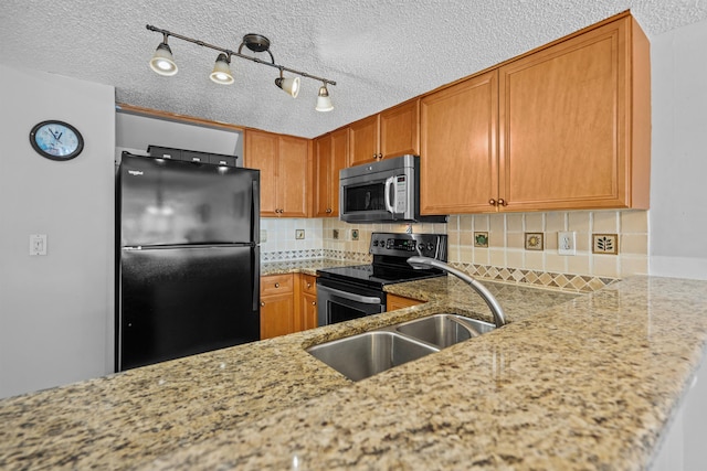 kitchen with appliances with stainless steel finishes, track lighting, light stone counters, and decorative backsplash