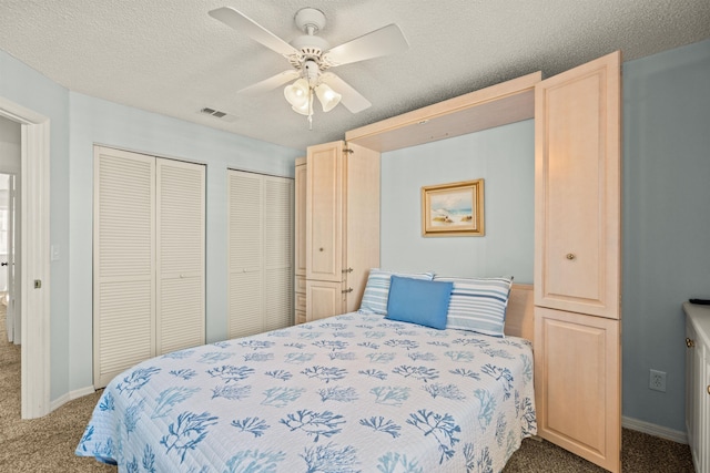 bedroom featuring multiple closets, carpet floors, a textured ceiling, and ceiling fan