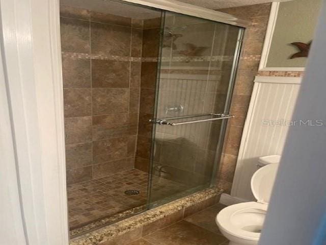 bathroom with tile patterned flooring, a shower with shower door, and toilet