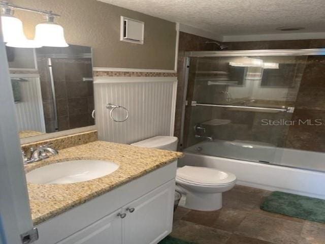 full bathroom with combined bath / shower with glass door, vanity, a textured ceiling, and toilet