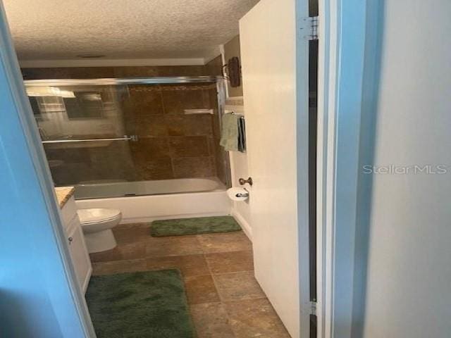 full bathroom with vanity, bath / shower combo with glass door, a textured ceiling, and toilet