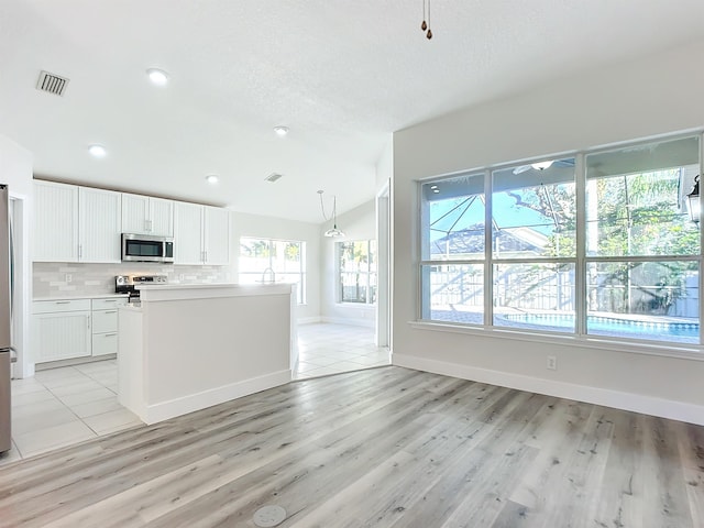 kitchen featuring pendant lighting, lofted ceiling, appliances with stainless steel finishes, light hardwood / wood-style floors, and white cabinetry