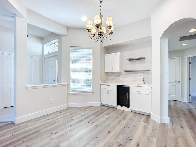 bar featuring beverage cooler, pendant lighting, light hardwood / wood-style flooring, a chandelier, and white cabinetry