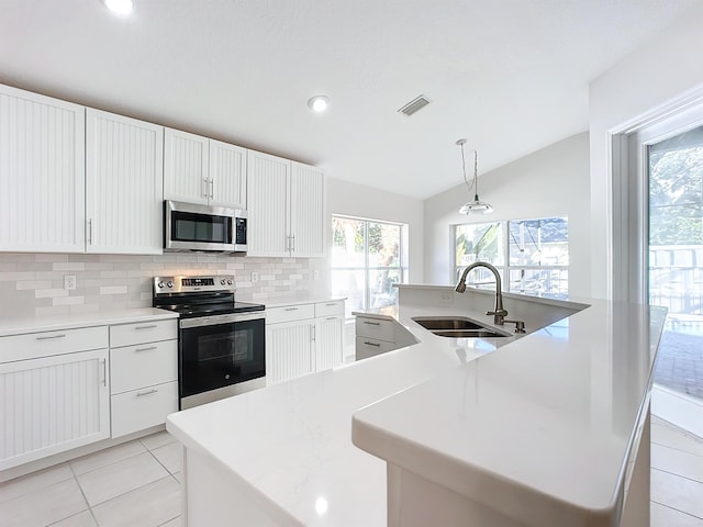 kitchen featuring sink, stainless steel appliances, decorative light fixtures, lofted ceiling, and a center island with sink