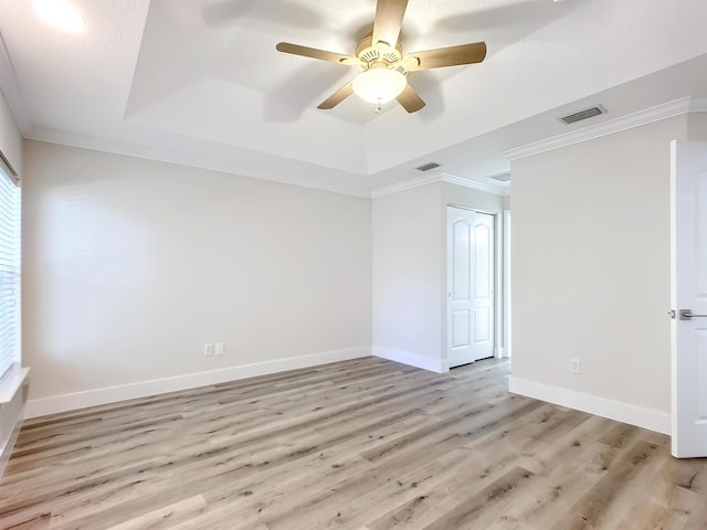 empty room with light wood-type flooring, a raised ceiling, ceiling fan, and crown molding