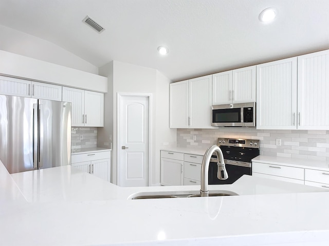 kitchen featuring appliances with stainless steel finishes, backsplash, vaulted ceiling, sink, and white cabinets