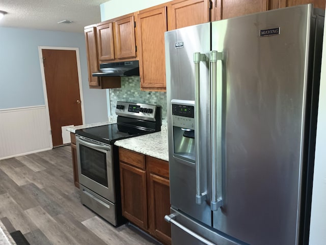 304 Las Olas Rd, Saint Augustine, FL 32084 - kitchen with appliances with stainless steel finishes, under cabinet range hood, light wood-type flooring, a wainscoted wall, and a textured ceiling