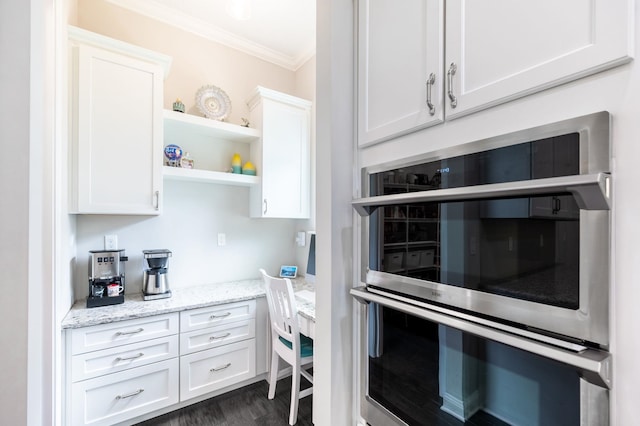 kitchen featuring light stone countertops, stainless steel double oven, dark wood-type flooring, white cabinets, and ornamental molding