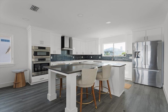 kitchen with visible vents, a center island, wall chimney range hood, appliances with stainless steel finishes, and white cabinets