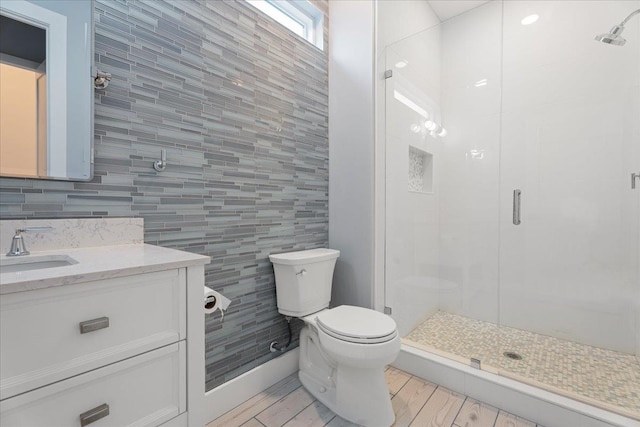 bathroom with toilet, wood finished floors, tile walls, a shower stall, and vanity