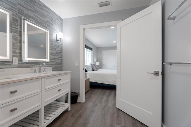 ensuite bathroom featuring ensuite bath, wood finished floors, visible vents, and a sink