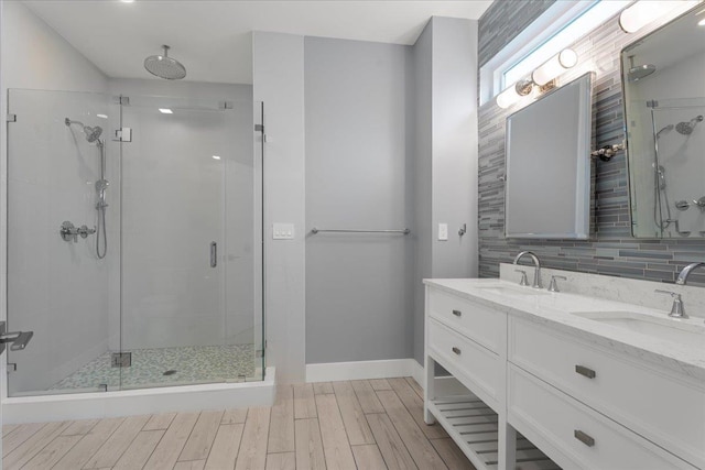 bathroom featuring wood finished floors, double vanity, a stall shower, a sink, and backsplash