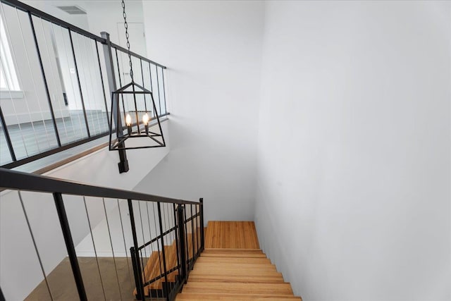 stairs with an inviting chandelier, wood finished floors, and visible vents