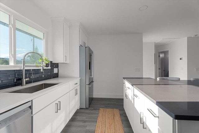 kitchen with dark wood-type flooring, decorative backsplash, stainless steel appliances, white cabinetry, and a sink