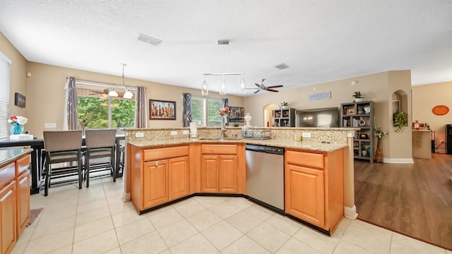 kitchen featuring stainless steel dishwasher, ceiling fan, sink, hanging light fixtures, and an island with sink