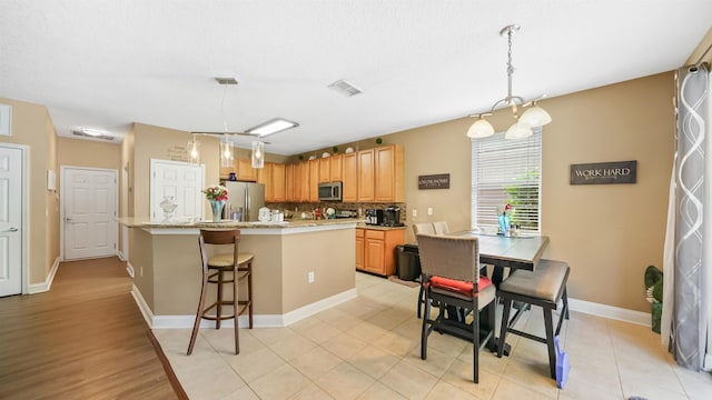 kitchen with stainless steel appliances, light stone counters, pendant lighting, decorative backsplash, and light tile patterned floors