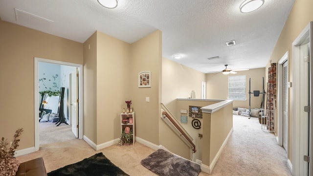 hall with light colored carpet and a textured ceiling