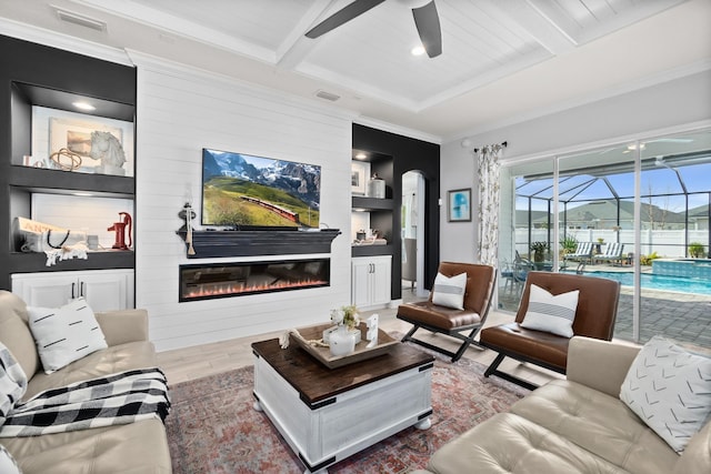 living room with beam ceiling, hardwood / wood-style floors, a fireplace, ceiling fan, and crown molding