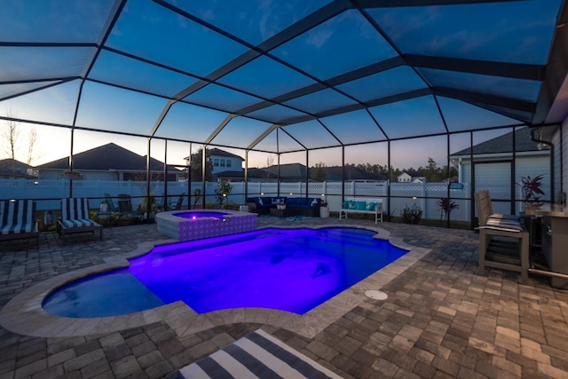 pool at dusk with an in ground hot tub, a lanai, and a patio