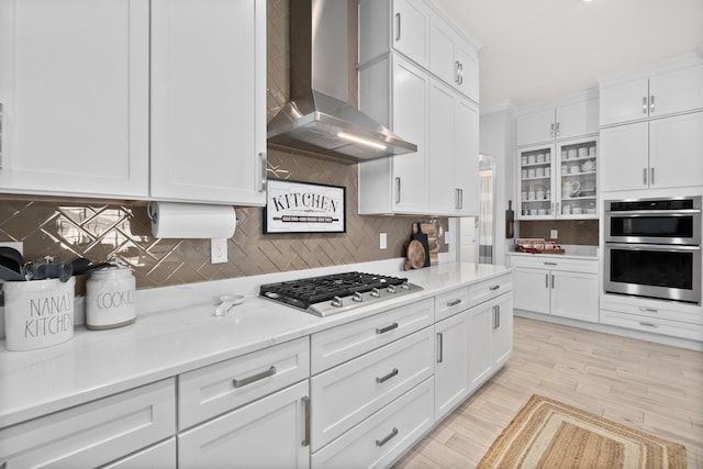 kitchen featuring wall chimney exhaust hood, backsplash, white cabinetry, light stone countertops, and stainless steel appliances