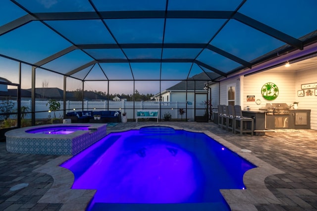 pool at dusk with glass enclosure, an in ground hot tub, a patio area, a grill, and an outdoor kitchen