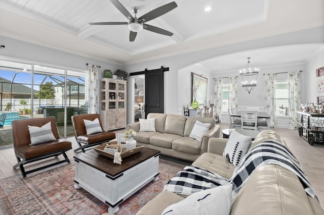 living room featuring wood-type flooring, a barn door, ceiling fan with notable chandelier, ornamental molding, and beamed ceiling