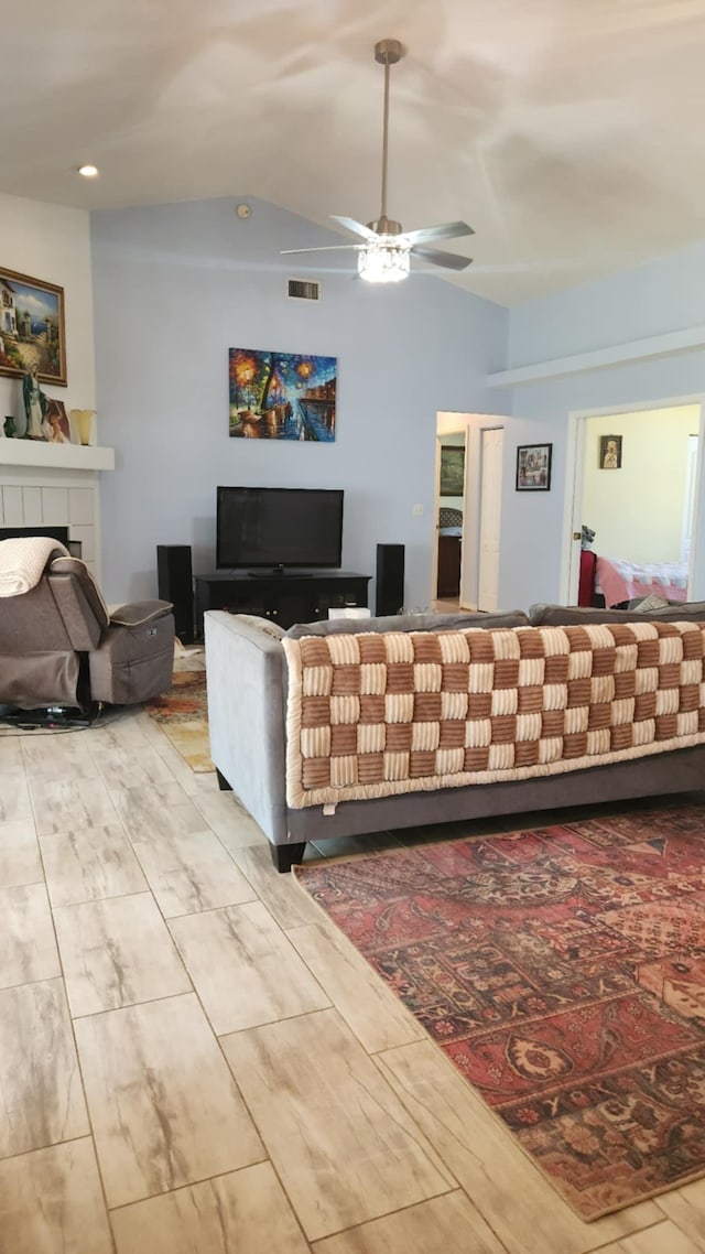 living area featuring a tiled fireplace, visible vents, ceiling fan, and lofted ceiling