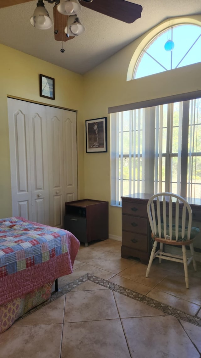 tiled bedroom with a closet, ceiling fan, baseboards, and lofted ceiling