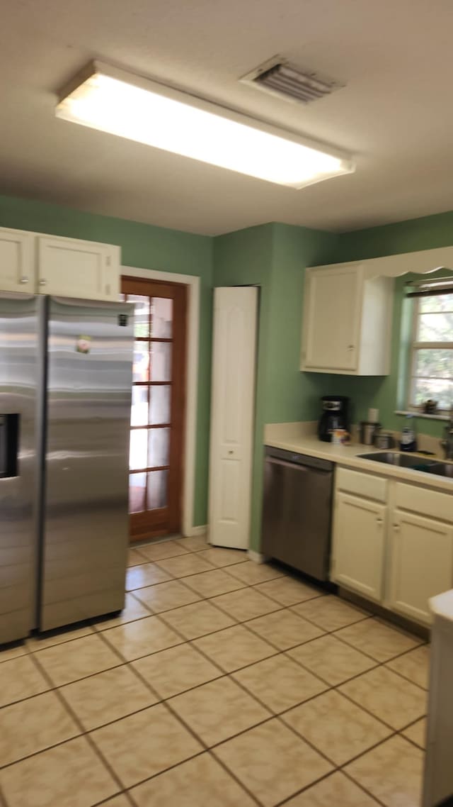 kitchen with visible vents, a sink, appliances with stainless steel finishes, white cabinets, and light tile patterned floors