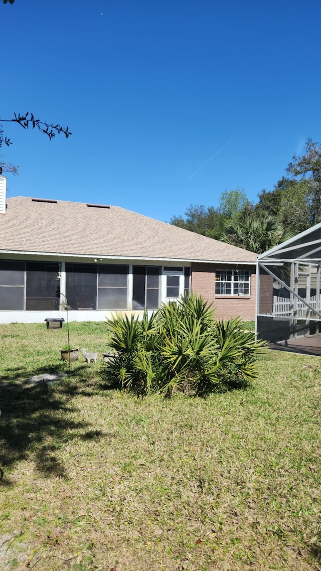 view of side of property with brick siding, a lawn, roof with shingles, and a sunroom