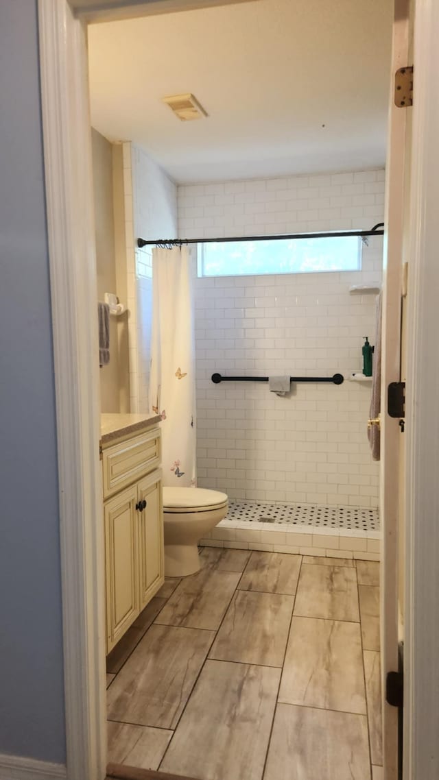 full bathroom featuring visible vents, tiled shower, toilet, and vanity