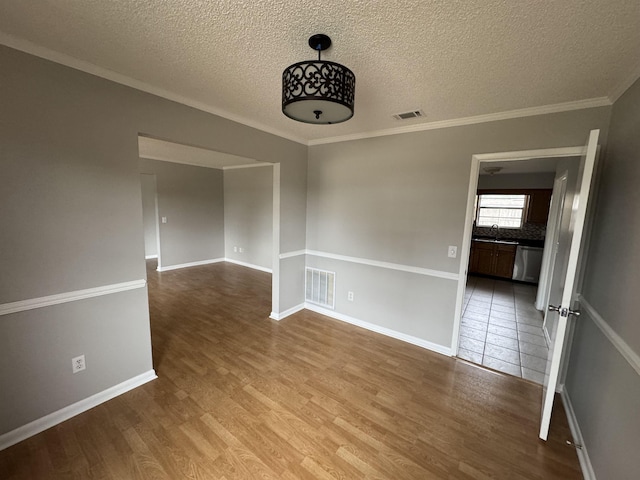 empty room featuring sink, ornamental molding, hardwood / wood-style floors, and a textured ceiling