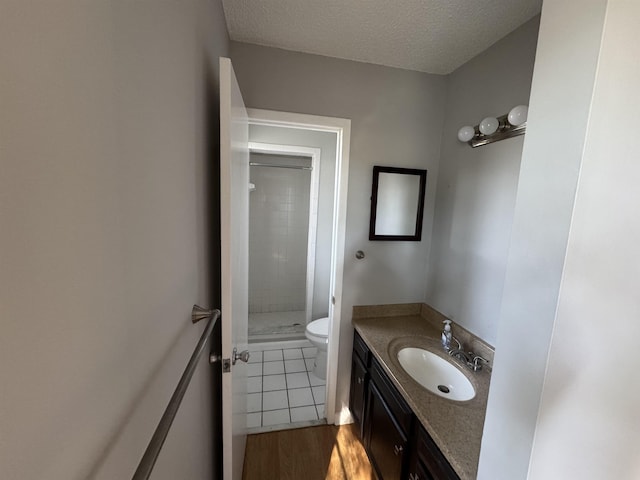 bathroom with tiled shower, vanity, wood-type flooring, a textured ceiling, and toilet