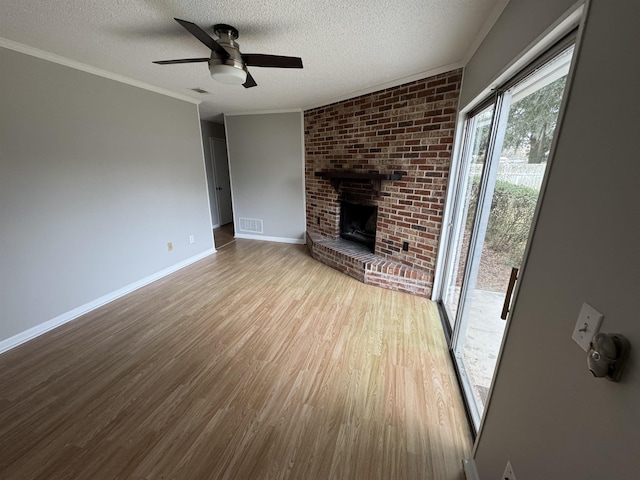 unfurnished living room featuring a brick fireplace, a textured ceiling, ornamental molding, ceiling fan, and light hardwood / wood-style floors