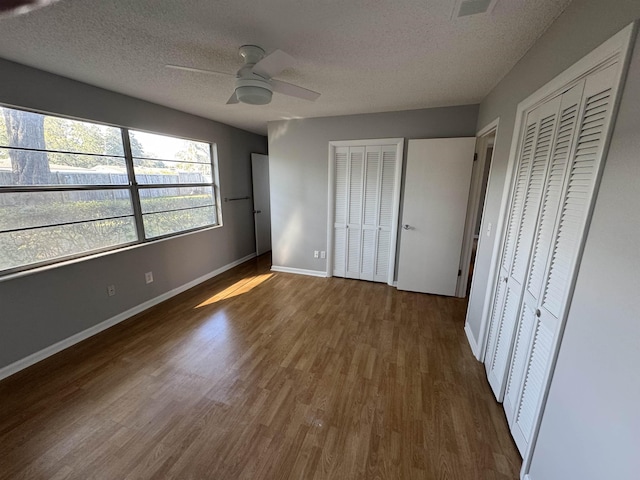 unfurnished bedroom featuring ceiling fan, a textured ceiling, dark wood-type flooring, and multiple closets