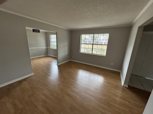 empty room featuring crown molding, a textured ceiling, a wealth of natural light, and wood-type flooring