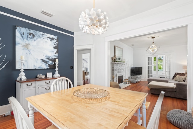 dining area with ornamental molding, a brick fireplace, an inviting chandelier, and light hardwood / wood-style flooring