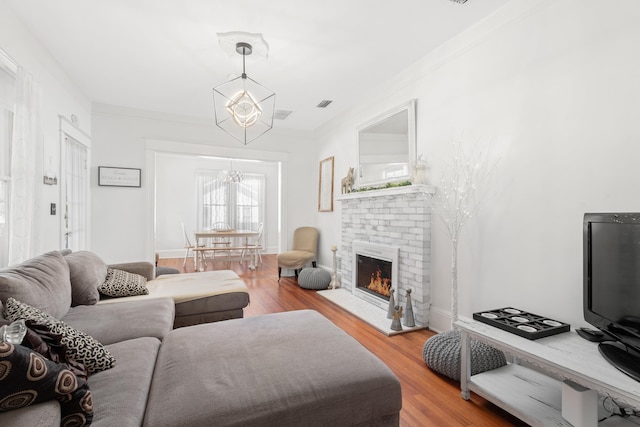 living room with a chandelier, wood-type flooring, a brick fireplace, and ornamental molding