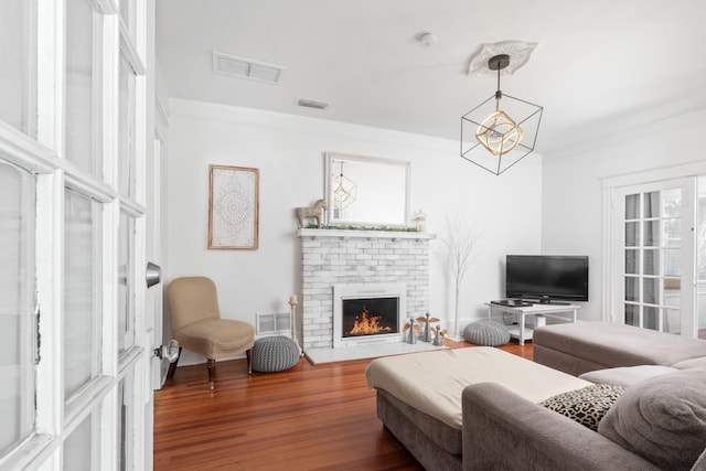 living room with hardwood / wood-style flooring, a brick fireplace, ornamental molding, and a notable chandelier