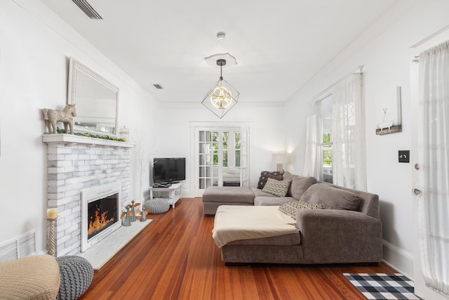 living room featuring hardwood / wood-style floors, an inviting chandelier, a brick fireplace, and ornamental molding