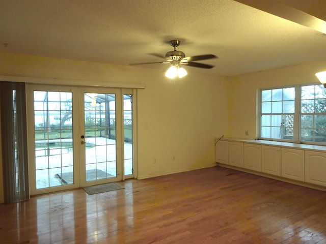 unfurnished room featuring light wood finished floors, a ceiling fan, a textured ceiling, and french doors